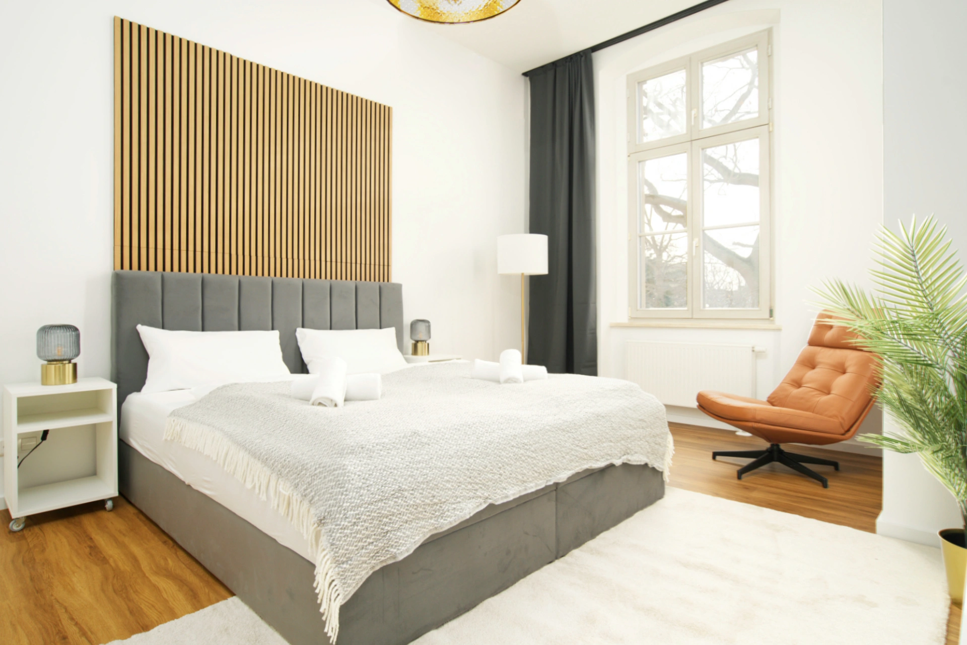 Blick in ein Schlafzimmer mit Doppelbett mit weißer Bettwäsche einem Sessel und Akustikpaneele an der Wand